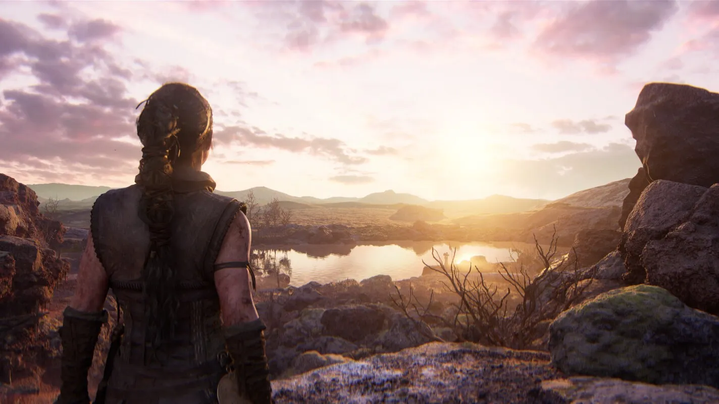 Senua, de espaldas, mira un lago entre rocas al atardecer