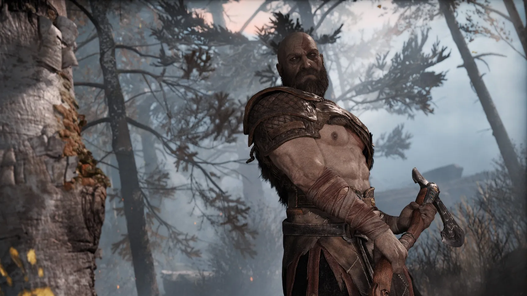 Kratos, con el hacha en la mano, en un bosque con niebla junto a un árbol marcado con una mano amarilla