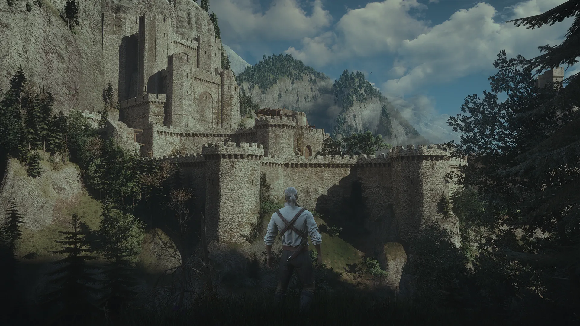 Geralt, de espaldas, mira una fortaleza de piedra entre montañas